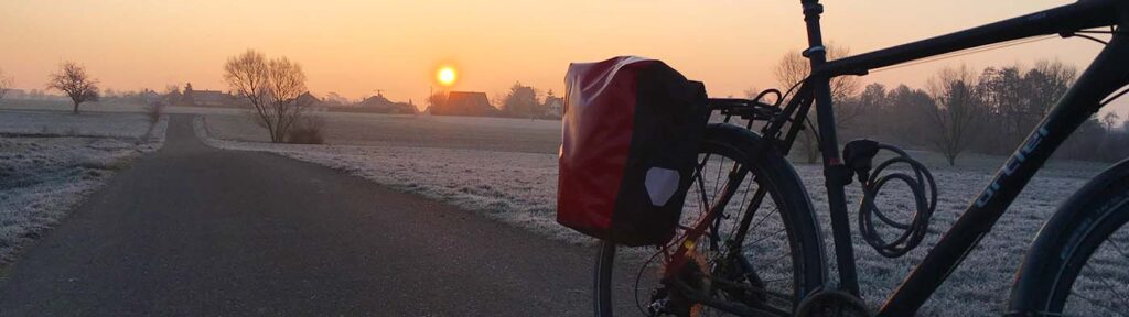Ein Fahrrad mit einer Hinterradtasche von Ortlieb bei aufgehender Sonne im Winter