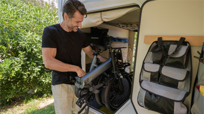 Ein Mann verstaut sein eingeklappetes Faltrad in ein Wohnmobil.